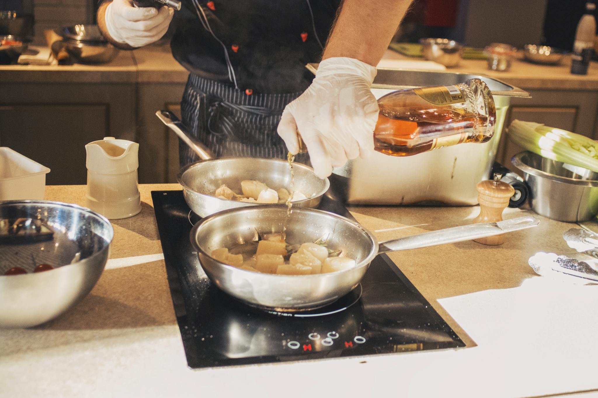 A chef adds whiskey to sautéing scallops in a professional kitchen setting.