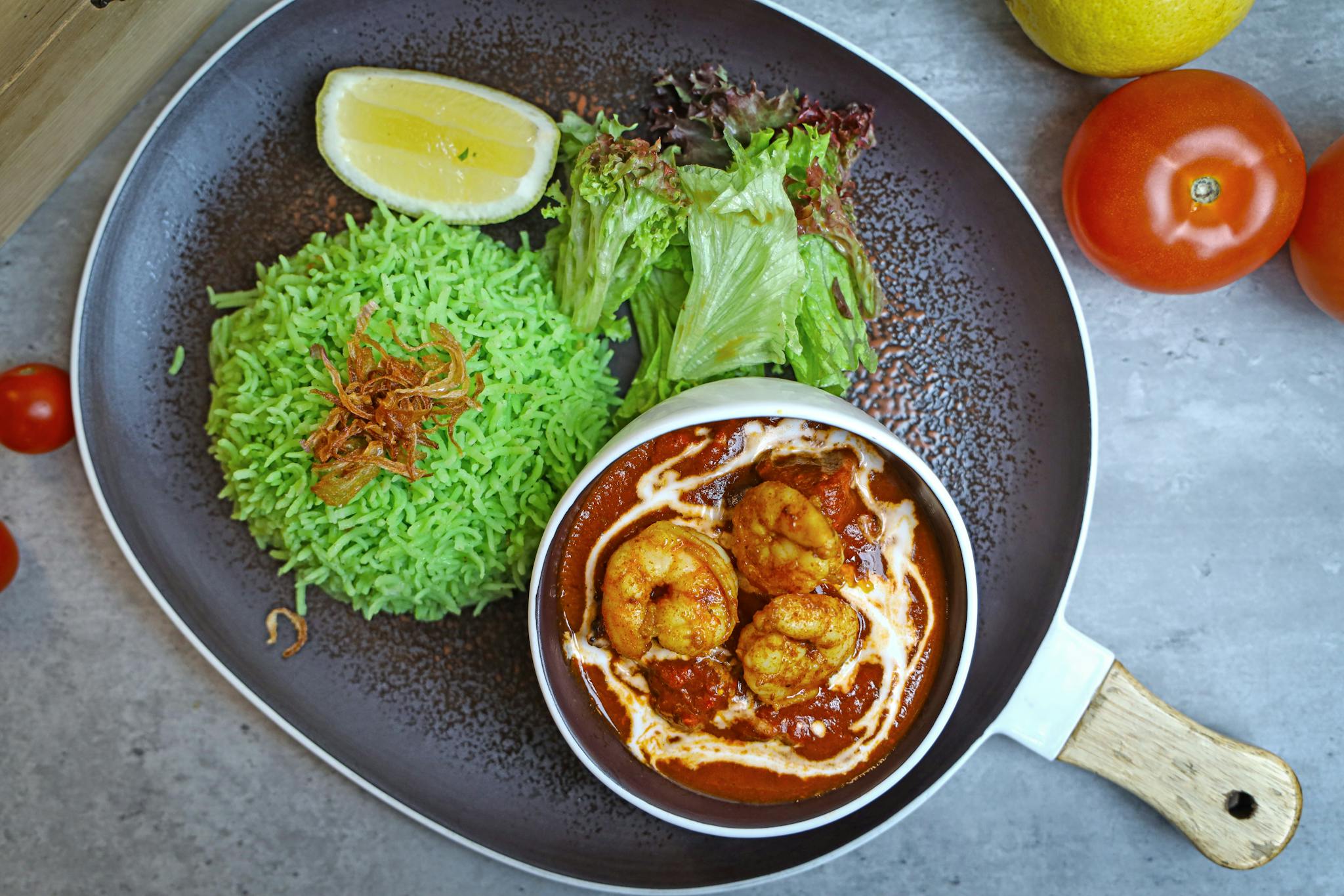 A delicious plate featuring spicy shrimp curry, green rice, and fresh salad with a lemon wedge.